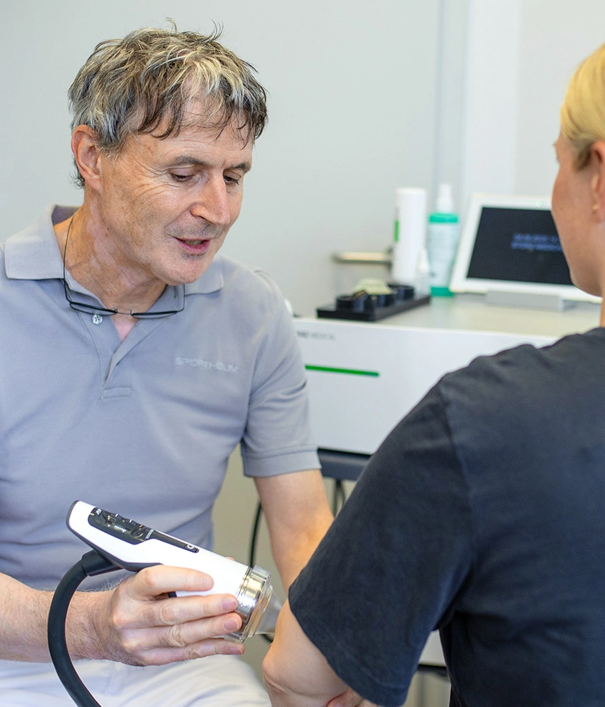 Sportheum_Sportklinik_Fellbach_Leistungen_Therapie_Konservative_Operative Behandler der Sportheum Sportklinik Fellbach wendet ein modernes Therapiegerät am Ellenbogen einer Patientin an – konservative Behandlungsmethoden auf dem neuesten Stand der Technik.